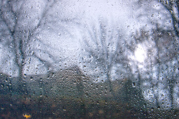 View of the autumn rainy city blurred landscape from the car through the glass covered with rain drops. Focus on water droplets