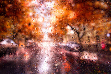 View of the autumn rainy city blurred landscape from the car through the glass covered with rain drops. Focus on water droplets