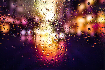 City view through a window on a rainy night,Rain drops on window with road light bokeh, City life in night in rainy season abstract background. Focus on drops on glass	 - obrazy, fototapety, plakaty