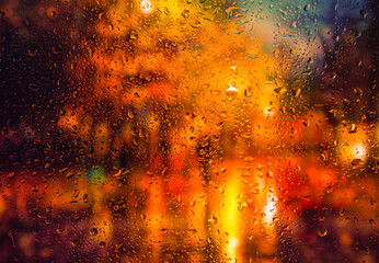 Fototapeta na wymiar City view through a window on a rainy night,Rain drops on window with road light bokeh, City life in night in rainy season abstract background. Focus on drops on glass 
