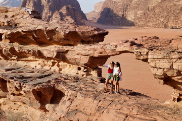 close view of two tourists on rocks visiting wadi rum desert - obrazy, fototapety, plakaty