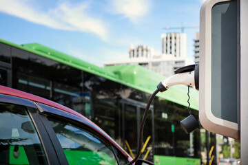 Passenger vehicles are being charged against the background of a passing green bus with passengers.