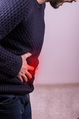 Man suffering with severe stomach pain sitting at home. Hand of mature guy holding abdomen...