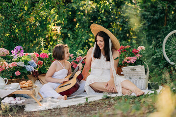 Beautiful mother and daughter family on picnic with guitar at summer spring sunny day