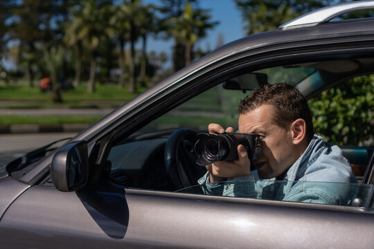 Paparazzi men or guy in sunglasse sits in her car and takes pictures of famous person.Spy with camera in car. Private detective or paparazzi journalist sitting inside car, taking pictures with camera.