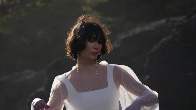 Beautiful Woman In Simple Elegant White Dress With Dangler Earrings Posing Outdoor In Sunlight. medium shot