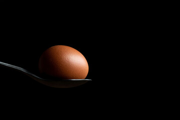 brown hen's egg photographed on a dinner spoon, egg photo, egg close-up, brown egg isolated on black backround

