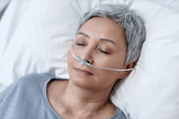 High angle view of unconscious mature woman breathing artificially through a tube lying on bed in ward