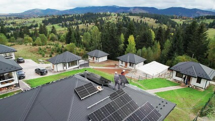 Technicians building solar panel system on roof of house. Drone view of men workers in helmets carrying photovoltaic solar module outdoors. Concept of alternative and renewable energy.