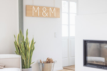 Wohnzimmer im modernen skandinavischen Stil mit Kamin, Feuerholz, Kunst, Leuchtschtrift an der Wand, Neon-Buchstaben, einer Pflanze, einem Sofa und hellen weißen Wänden