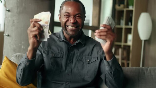 Portrait of mature african american man counting stack of dollars banknotes at home alone Successful male holding money show to camera and rejoices at good earnings income salary indoors