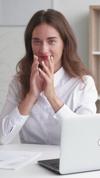 Vertical video. Evil plan. Office woman. Ironic expression. Smiling lady running fingers in malicious joy sitting work desk light room interior.