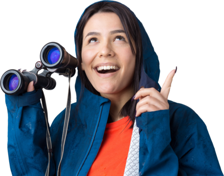 A tourist girl in a blue raincoat holds binoculars in her hands and looks into the distance, spies.