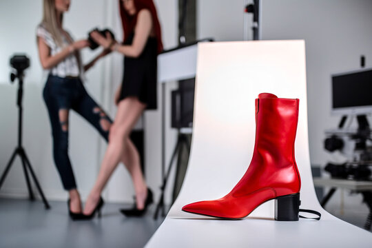 Red women's boot in a photo studio for product photography with female photographer out of focus in the background, made with generative ai