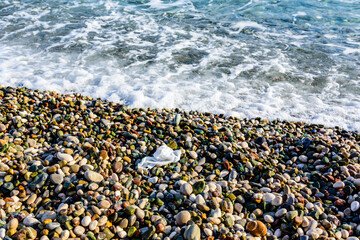 A disposable face mask discarded on pebble at the beach