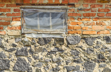 Window is covered with oilcloth. A wall of red brick and gray stone.