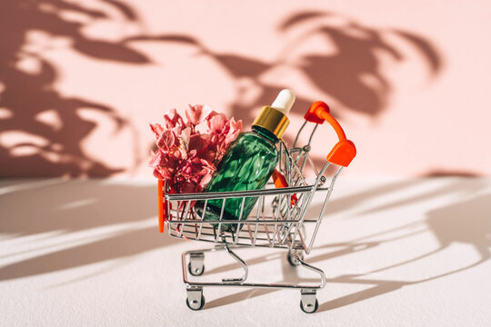 Face serum in shopping cart on pink background.