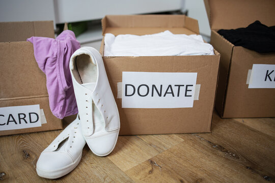 Close up clothes being sorted into of boxes Keep, Discard, Donate categories white sneaker. Zero Waste, recycling, sustainable. Decluttering and aleaning up closet or wardrobe