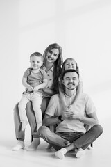 Young happy mother, father embrace child daughter and son isolated in background studio. Parents hug children relaxing on a sofa on a wall at home. Family moving into new house. Black and white photo.