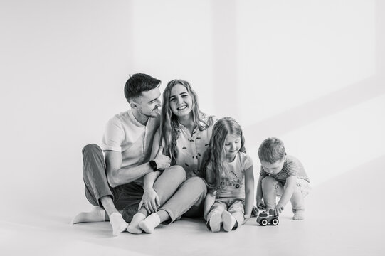 Family moving into new house. Relocation concept. Young happy mother, father with child daughter, son isolated on wall. Funny parents hug children sit, relaxing on floor at home. Black and white photo