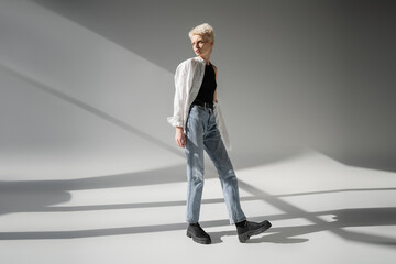 full length of albino woman in black tank top and white shirt posing on grey background with shadows.
