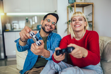 Boyfriend and girlfriend playing video game with joysticks in living room. Loving couple are playing video games at home.