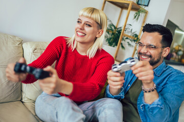 Boyfriend and girlfriend playing video game with joysticks in living room. Loving couple are playing video games at home.