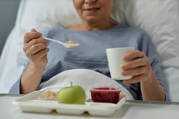 Close-up of senior patient sitting on bed with tray and eating healthy food during lunch