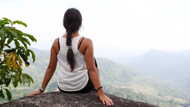 A Girl Sits On A Rock On Top Of A Mountain, View From Behind