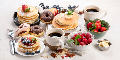 Pancakes with fresh fruits, donuts and coffee on a white background.