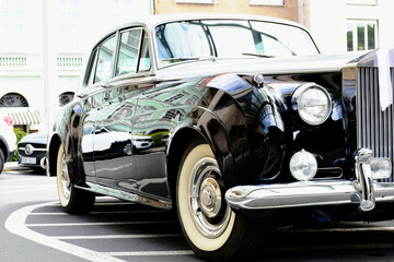 classic old British made elegant and expensive car closeup. headlights and shiny side panel. white walled rubber tires. wedding and marriage concept. ribbon on front grille. soft blurred background. 