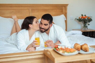 Obraz na płótnie Canvas Wife Kissing Husband Enjoying Breakfast In Bed In Hotel Suite