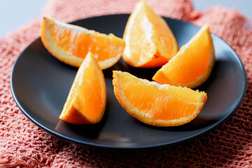 Fototapeta na wymiar Orange slices on black plate, closeup. Selective focus