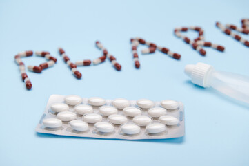 Fototapeta na wymiar Selective focus on a blister with white pharmaceutical pills over blue background with capsules laid out in the word pharmacy. Pharma business and industry. Healthcare amd medicine. World Health Day