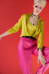 albino model with tattooed hand posing in stylish blouse and pink sunglasses on carmine background.