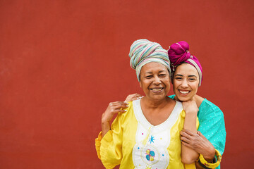 Happy african mother and her daughter wearing ethnic afro clothes while smiling in front of camera - Mom day, family and love concept - obrazy, fototapety, plakaty