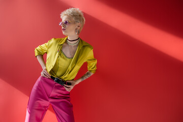 young albino model with tattoo on hand posing in stylish blouse and trendy sunglasses on carmine...