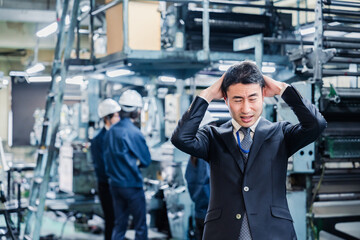 工場で頭を抱えるスーツの男性