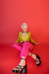 full length of young model in trendy clothes and heeled sandals posing on carmine pink background.