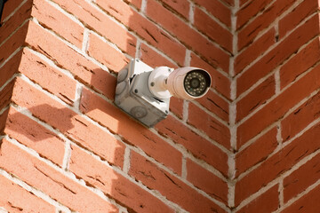 Small white CCTV camera on the corner of the facade of a multi-storey brick building. Security...