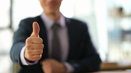 Manager businessman showing gesture thumb up at work in office closeup. Victory and successful strategy in business concept