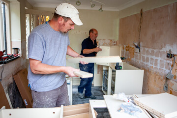 Kitchen Fitters: Flat Pack Build. A pair of carpenters building the carcass to a new fitted kitchen. From a series of related images.