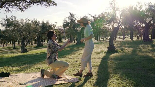Wide shot slow motion homosexual marriage proposal gay lgbt exciting on a picnic in the park with sunset sunlight