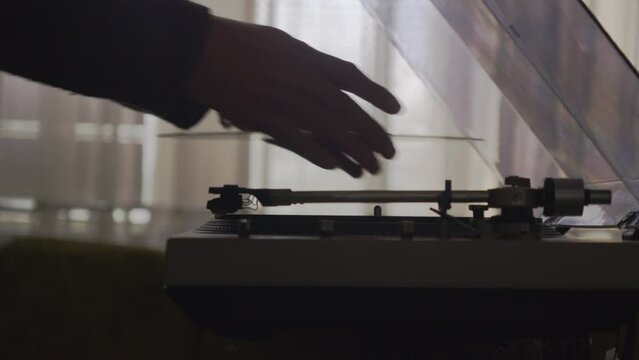 Silhouetted person flips vinyl record, plays music, and looks at cover. Loopable shot