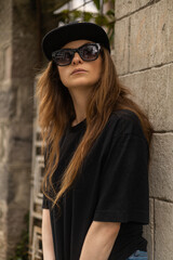 details of the face of a latin woman with long hair, she wears a hat, sunglasses, t-shirt, casual and youth fashion in the city