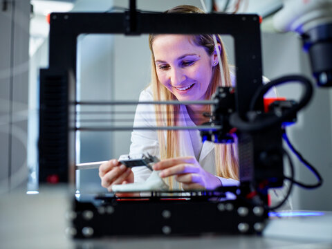 Smiling engineer holding vernier calliper operating 3D printing machine in laboratory