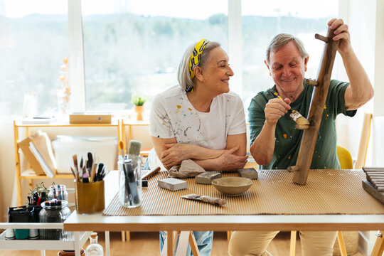 Smiling senior woman looking at man polishing wood in workshop