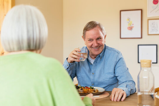 Smiling senior man with glass of water enjoying lunch at home