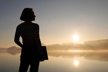 Silhouette of freelancer standing with laptop in front of lake