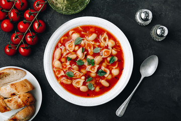 Tomato soup. Minestrone soup. Tomato bean and pasta soup bowl with toasts on dark stone background.